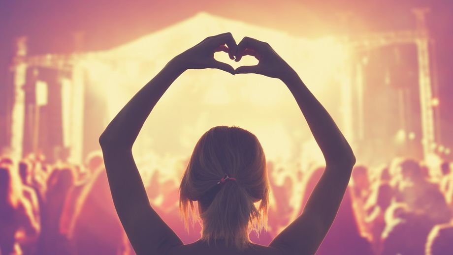 Frau macht Herzform mit Händen in Konzertmenge