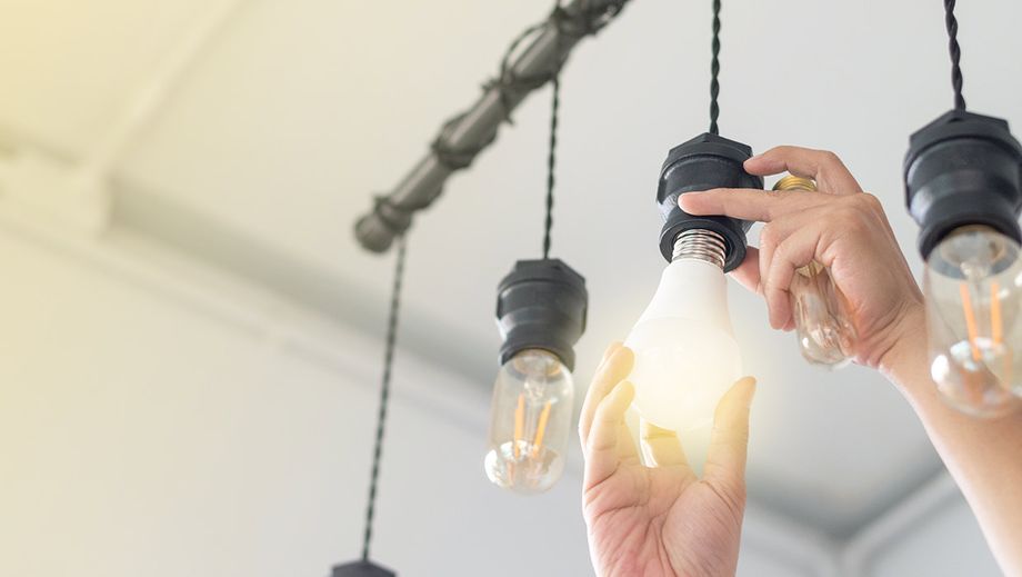 Person tauscht Glühbirne an einer Deckenlampe