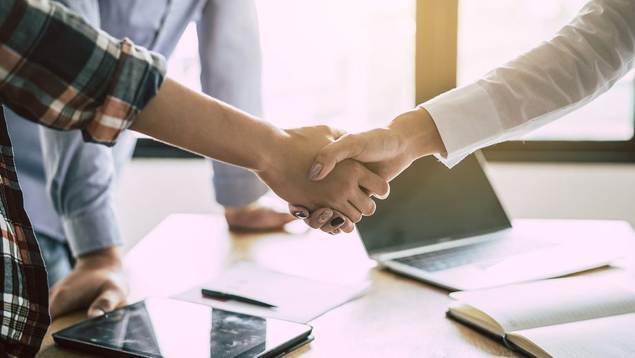 Zwei Personen schütteln sich über einen Tisch die Hände.