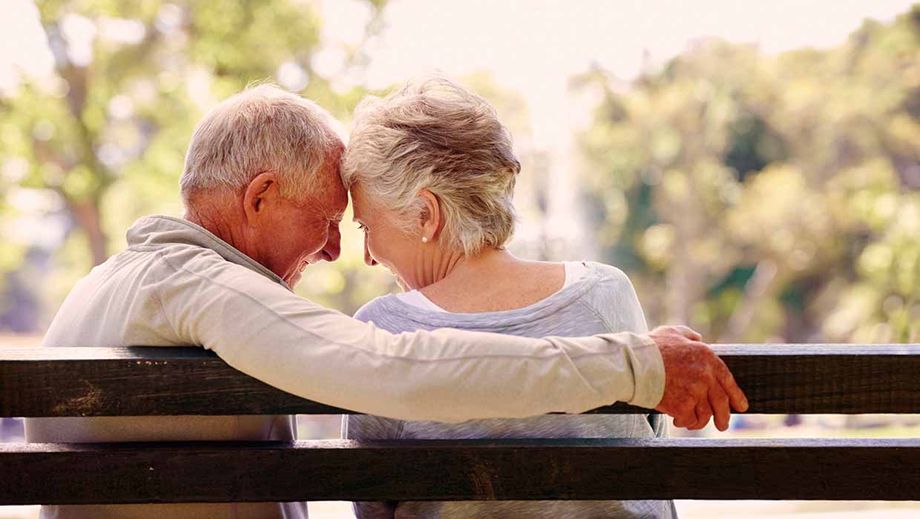 Älteres Paar kuschelt auf Parkbank