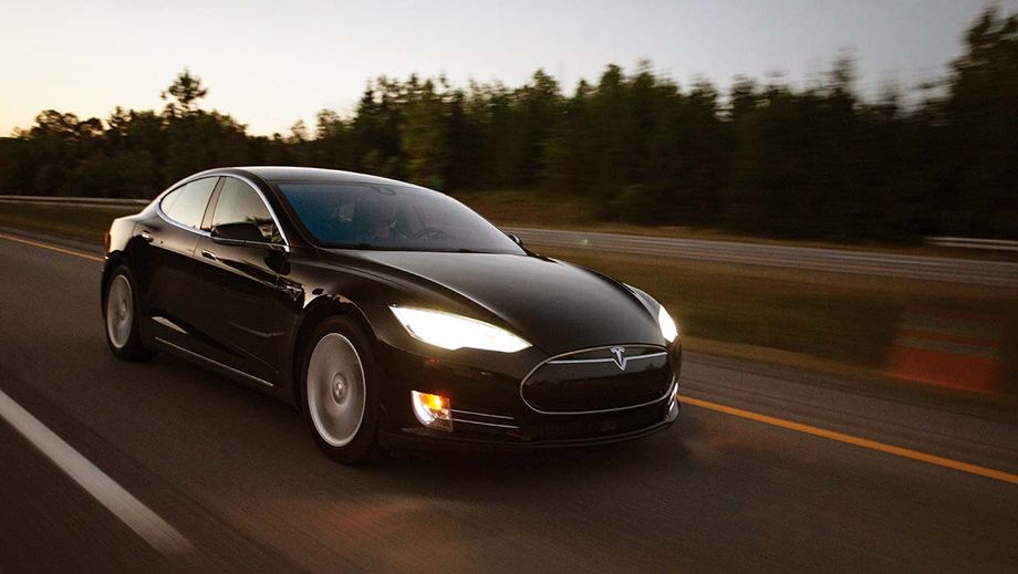 Schwarzes Elektroauto mit eingeschalteten Scheinwerfern