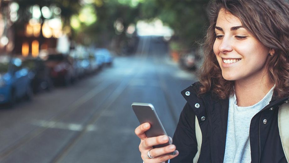 Person geht über die Straße und schaut auf ihr Smartphone.